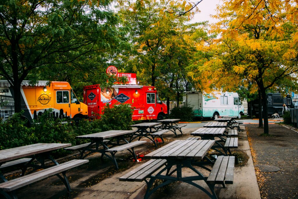 food trucks are parked at a park near benches and trees